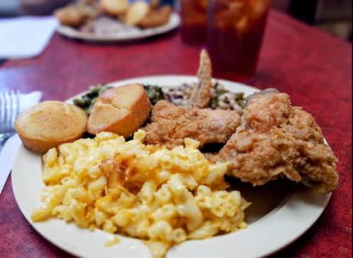 A plate of fried chicken, macaroni and cheese, cornbread, greens, and black-eyed peas on a red table.