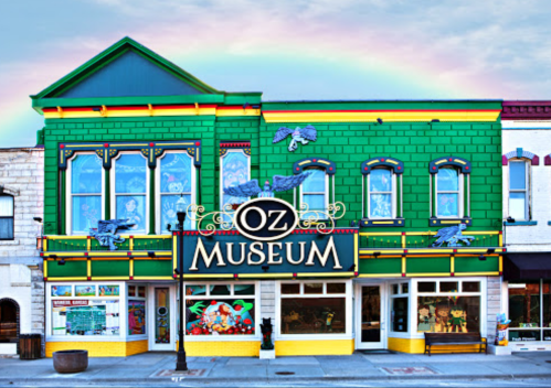 Colorful exterior of the Oz Museum, featuring green and yellow walls, large windows, and a rainbow in the background.
