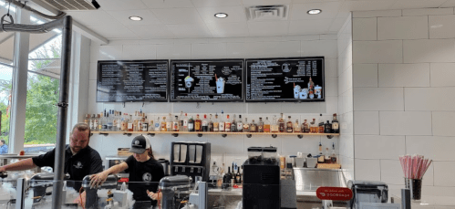 A modern ice cream shop interior with two staff members, a menu on screens, and a shelf of liquor bottles.