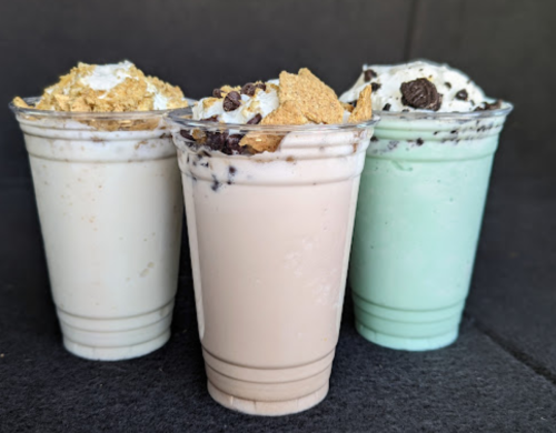 Three milkshakes in clear cups: one vanilla, one chocolate, and one mint, all topped with whipped cream and crumbs.