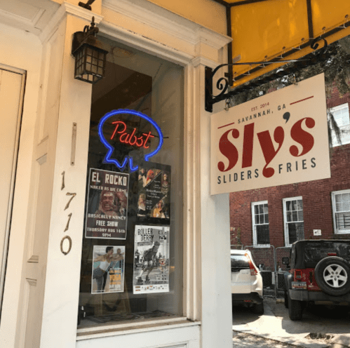 A storefront featuring a neon Pabst sign and a sign for Sly's Sliders & Fries in Savannah, GA.