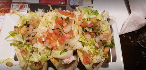 Three tacos filled with lettuce, diced tomatoes, and onions, served on a white plate.
