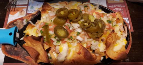 A sizzling platter of nachos topped with melted cheese, jalapeños, diced tomatoes, and onions.