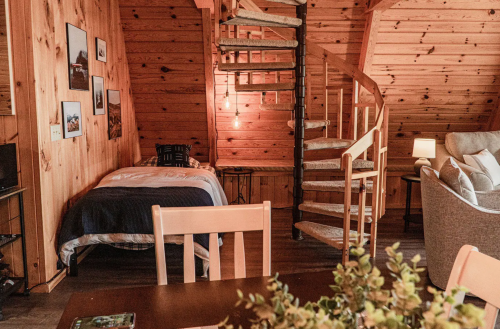 Cozy wooden interior featuring a spiral staircase, a bed, and a seating area with warm lighting.