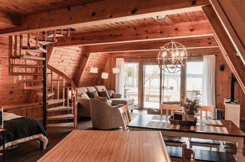 Cozy wooden interior of a cabin with a spiral staircase, living area, and large windows overlooking a lake.