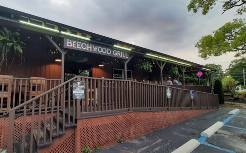 Exterior of Beechwood Grill, featuring a wooden structure, outdoor seating, and a cloudy sky in the background.