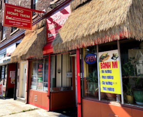 Exterior of Pho Hong Thom restaurant with a thatched roof, open sign, and a menu displayed in the window.