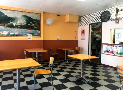 A small, empty restaurant with checkered floors, wooden tables, and a mural of mountains on the wall.