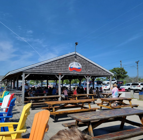 Outdoor dining area with colorful chairs, wooden tables, and a shaded pavilion under a clear blue sky.