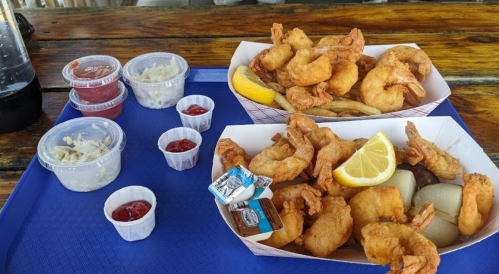 Two trays of fried shrimp with lemon, accompanied by dipping sauces and sides on a blue tray.