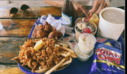 A tray of food featuring fried seafood, fries, potato chips, coleslaw, and a drink, with sunglasses in the background.