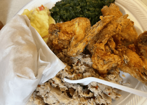 A plate of fried chicken, shredded meat, sautéed greens, and a side of mashed potatoes, served with a napkin.