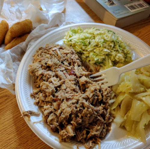 A plate with shredded meat, coleslaw, cooked cabbage, and a side of fried snacks, with a fork and a glass of water.