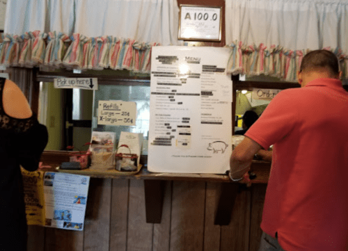 A menu board displayed at a counter with two people ordering, surrounded by colorful decorations and signs.
