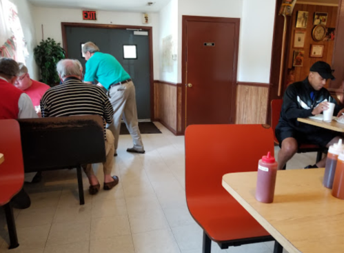 A casual diner scene with patrons at tables, condiments on the table, and a man walking towards the exit.