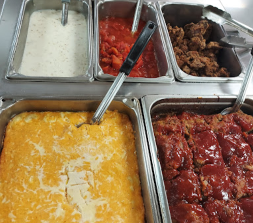 A buffet with five trays of food: creamy sauce, diced tomatoes, shredded cheese, meatloaf, and seasoned meat.