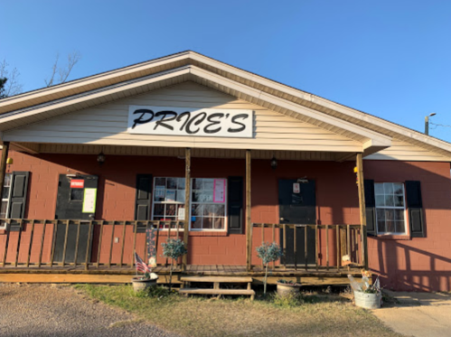 A small, rustic building with a sign reading "PRICE'S" and a wooden porch, surrounded by greenery.