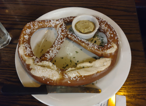 A large, soft pretzel sprinkled with salt, served with a small dish of mustard on a white plate.