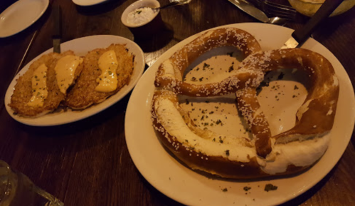 A large salted pretzel on a plate next to two fried items topped with sauce.