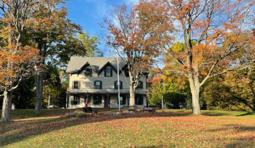A large house surrounded by colorful autumn trees and fallen leaves on a sunny day.