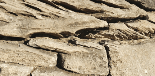 Close-up of textured, weathered stone wall with layered rock formations and natural color variations.
