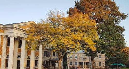 A historic building with columns beside vibrant autumn trees in a serene setting.