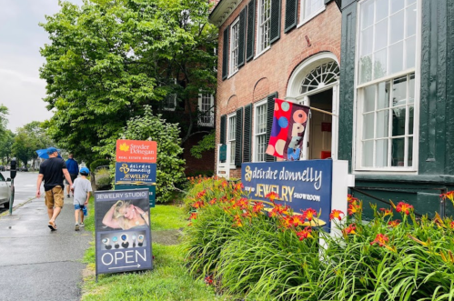 A couple walks past a jewelry store with colorful signs and vibrant flowers on a rainy day.