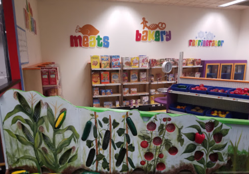 Colorful grocery store interior featuring sections for meats, bakery, and a refrigerator, with a mural of fruits and vegetables.