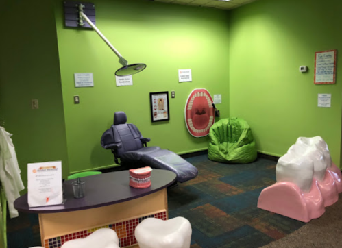 A colorful children's dental waiting area with bean bags, a dental chair, and playful decor on green walls.