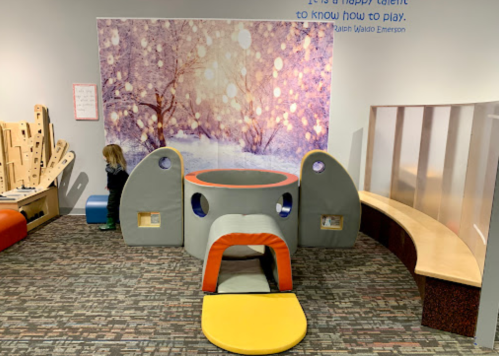 A colorful play area with soft structures, a circular playhouse, and a snowy backdrop, designed for children's activities.