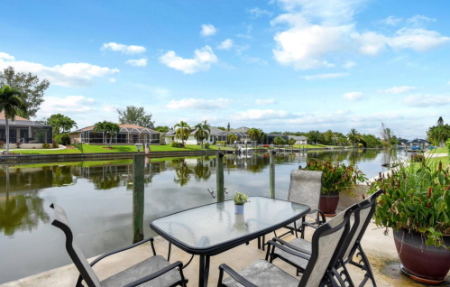 A serene canal view with a patio table and chairs, surrounded by lush greenery and waterfront homes.