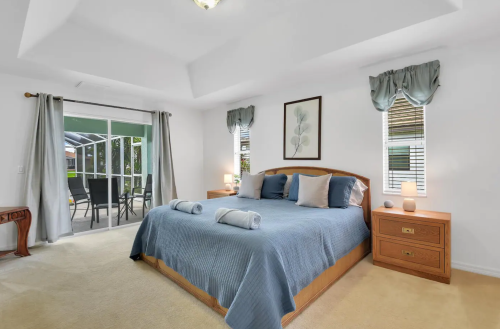 A cozy bedroom with a large bed, light blue bedding, and a view of a patio through sliding glass doors.