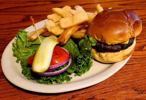 A juicy burger on a bun with lettuce, tomato, onion, pickles, served with a side of crispy fries on a plate.
