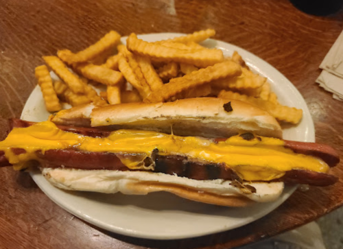 A hot dog with melted cheese in a bun, served with a side of crinkle-cut fries on a white plate.