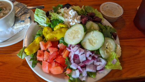 A colorful salad with lettuce, tomatoes, cucumbers, red onions, kidney beans, and pepperoncini, served with dressing.