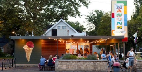 A charming ice cream shop with outdoor seating, string lights, and a colorful sign, bustling with customers.