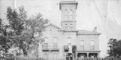 Historic building with a tall tower, intricate architecture, and surrounding trees, captured in a vintage style.