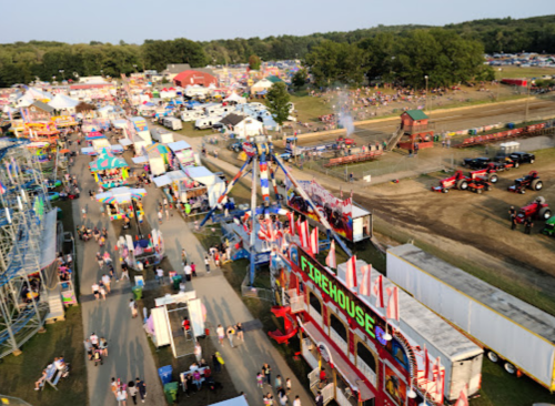 Aerial view of a lively fair with colorful tents, rides, and crowds enjoying various attractions and activities.