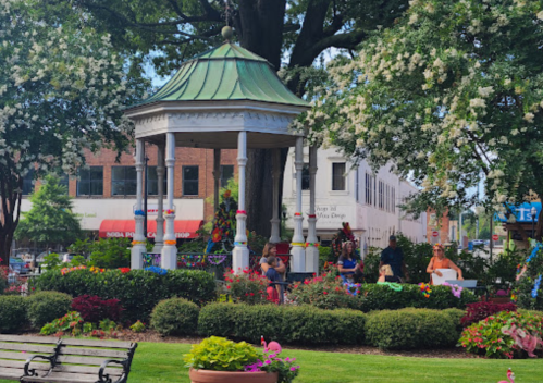 A charming gazebo surrounded by colorful flowers and people enjoying a sunny day in a park.