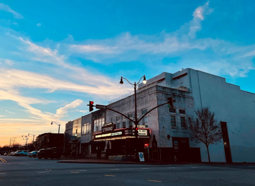 A vintage theater building at sunset, with colorful clouds and streetlights illuminating the scene.