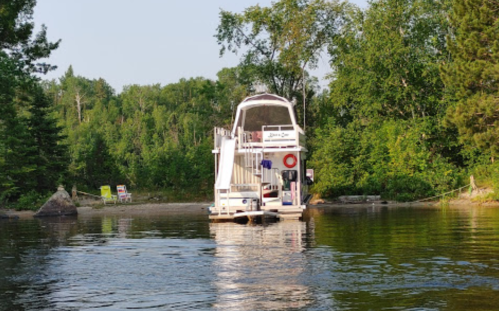 A boat docked near a forested shore, surrounded by calm water and greenery.