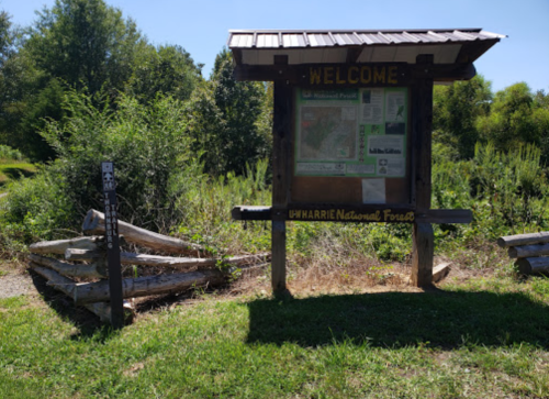Welcome sign for Uwharrie National Forest, surrounded by greenery and a trail marker nearby.