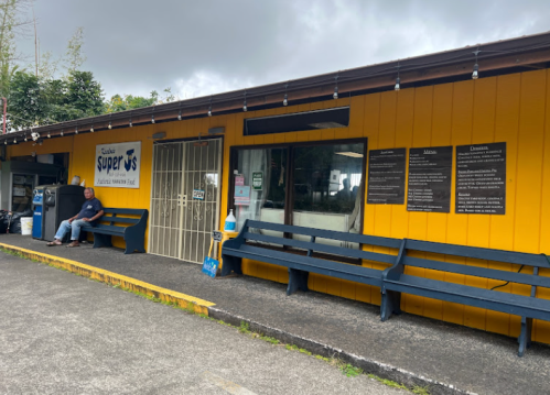 A yellow building with a sign reading "Super" and benches outside; a person sits nearby.