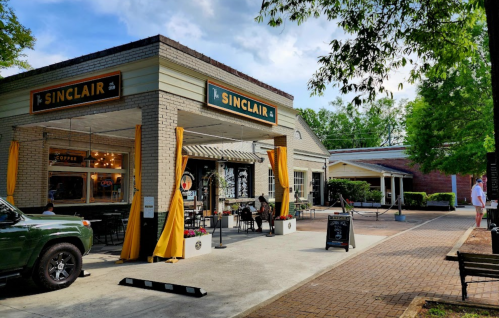 A charming café named Sinclair with outdoor seating, yellow curtains, and a welcoming atmosphere on a sunny day.