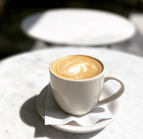 A latte in a white cup on a marble table, with a swirl design on the surface and a napkin underneath.
