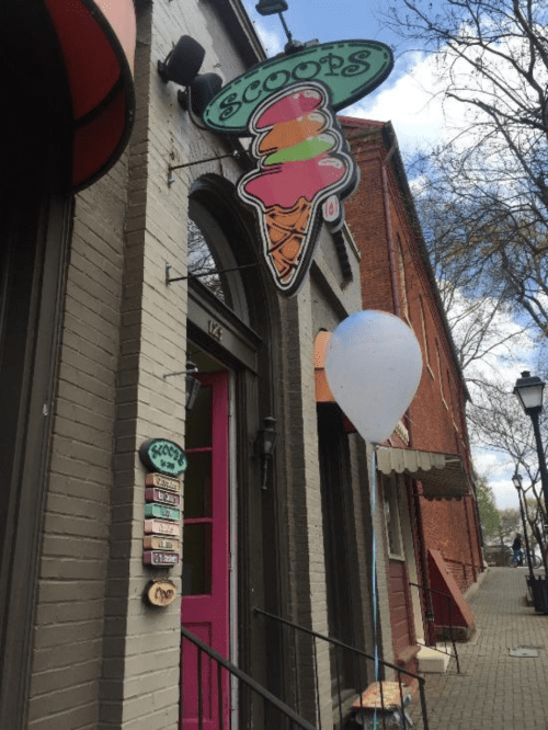 Colorful ice cream shop sign with a cone, pink door, and a white balloon outside on a charming street.