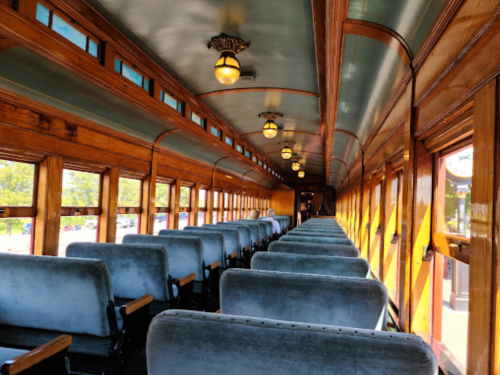 Interior of a vintage train car featuring wooden paneling and plush blue seats, illuminated by vintage-style lights.