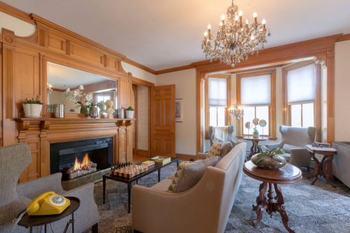 Cozy living room with wooden accents, a fireplace, elegant chandelier, and vintage decor, featuring a chess set and yellow phone.