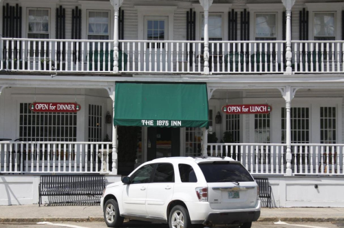 A white SUV parked in front of a historic inn with green awnings and signs indicating it's open for lunch and dinner.