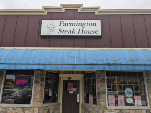 Exterior of Farmington Steak House with a blue awning, stone facade, and an "OPEN" sign in the window.